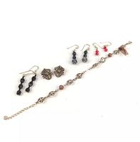 Five pairs of earrings with bracelet laid out on white background, showing variety in styles and materials.