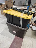 Two large plastic storage bins stacked with artificial Christmas tree parts on top, wrapped in plastic wrap.