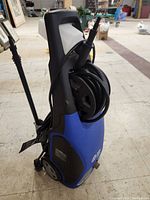 View of the AR Blue Clean power washer side showing hose reel, blue and black body, wheels at the base, and the handle at top.