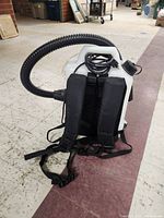Front view showing padded black shoulder straps and attached corrugated hose with power cord coiled on top