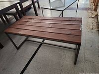 Oblique angle of bench showing wooden slat top with natural wood grain and black metal frame base.