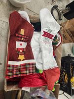Box containing multiple Christmas stockings with visible red and white stockings, one with a snowman design and plaid trim.