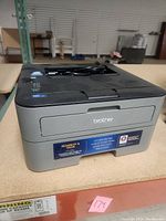 Front and top side view of Brother HL-L2320D laser printer on table showing brand, model, and power cable on top.
