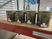 Four 1-gallon cans of GreenSheen paint in cream color arranged side by side on a shelf.
