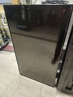 Front view of the 55-inch NEC E556 commercial display monitor screen, showing large black flat screen vertically propped on a floor.