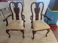 Front view of pair of wooden dining chairs showing carved backs, armrests, and upholstered seats.