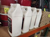 Four white plastic bottles of Rejuv One-Step Asphalt Enhancer & Protectant on a shelf, viewed from side and back angles.