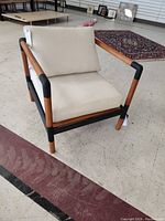 Front left angle view of armchair showing wooden frame, black corner supports, beige cushions.