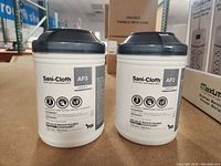 Front view of two white cylindrical containers of Sani-Cloth AF3 disposable wipes with gray lids showing product labels and instructions.
