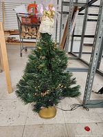 Full view of the small tabletop fiber optic Christmas tree showing green pine branches, golden base, and angel topper.