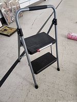 Front angle view of the Hyper Tough 2-step ladder showing the ribbed black plastic steps and padded handle grip.