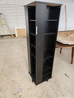 Full view of black swiveling tall shelving unit with a silver handle and visible holes for shelf adjustment.