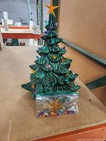 Green ceramic Christmas tree top with colorful mini lights embedded and a yellow star top visible. Bag of loose mini lights and topper placed in front.