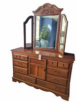 Full view of wood dresser with attached tri-fold mirror showing nine drawers and central door, carved details, and metal drawer handles.