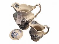 Photo showing two ceramic pitchers and a ceramic soap dish with lid, all decorated with blue floral patterns. The larger pitcher shows a small crack.