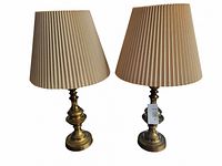 Photo of two solid brass table lamps with beige pleated shades, showing their turned bases and general condition.
