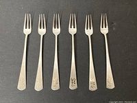 Six Korean silver condiment forks lined up flat on a black surface, showing the entire length and engraved handles.