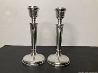 Pair of polished sterling silver candle sticks, each 8 inches tall, shown upright on a black surface.