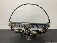 Front view of silver plated fruit bowl showing detailed Art Nouveau bird and leaf motifs and beaded handle.