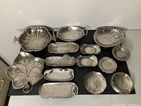 Full view of 14 pewter pieces including bowls, trays, and dishes arranged on a black surface showcasing various Art Nouveau designs.