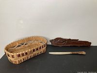 Overview photo showing the carved cedar piece, cedar root basket, and antique cutter knife together on a black surface against a white wall.