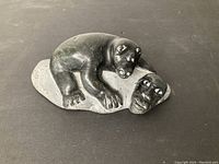 Top angled view of black stone carving showing bear resting over shaman face and torso.