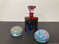 Photo showing two mille fleur paperweights and a multicolored Murano art glass perfume bottle with pink stopper.