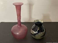 Pair of art glass vases showing a tall matte pink vase and a shorter black vase with beige swirls and silver rim.