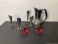All four items displayed together showing the pitcher, silver plated multi-arm candlestick, and two red painted candle holders.