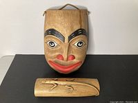 Photo showing the wood carved mask with painted facial features and the rectangular wood carving with a lizard design placed together