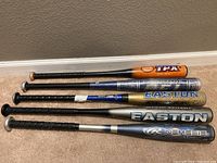 Five baseball bats lying on floor showing various colors, brands, and handles wrapped in grip tape.