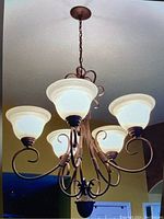 Front view of the bronze chandelier with five frosted glass lampshades. Shows chain, metal arms, and ornate design.