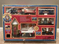 Image of Holiday Musical Express Christmas Train Set in original packaging showing locomotive, tender, passenger car, talking station, animated figures, and other festive accessories.