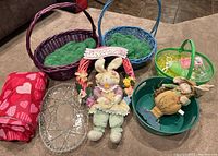 Photo showing three Easter baskets, two bunny decorations, a clear glass platter, a Valentine's Day tablecloth rolled, and a green plastic snowman container.