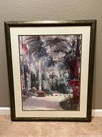 Photo of the framed tropical wall art showing the full piece including the dark wood frame, white matte, and detailed tropical scene inside.