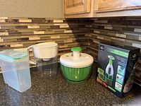 Photo of all kitchen items together: Sharper Image Chop 'N Store chopper with box, lettuce spinner, water filter container, and plastic storage container