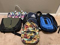 Overview photo showing all five bags: Case Logic laptop bag, colorful girls' rolling duffle, Adidas backpack, Five Star backpack, Madden Girl tropical backpack.