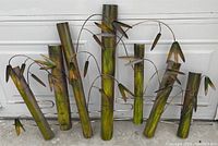Metal wall art piece designed like bamboo stalks with leaves in green and brown coloring, shown against a white background.