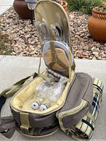 Rolling insulated duffel picnic bag open, showing plates, utensils, glasses, salt and pepper shakers, and attached blanket.