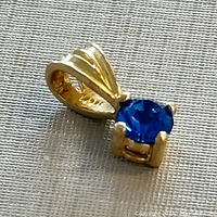 Close-up of the yellow gold pendant with blue gemstone showing the bail design and gemstone.