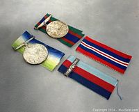 Photo showing two antique medals with their respective ribbons arranged on a flat surface, highlighting the ribbons' colors and medal shapes.