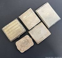 Four silver plate cigarette cases arranged on black background showing front designs and overall condition.