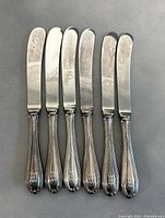 Six vintage sterling silver handle cheese spreaders arranged side by side showing the front of handles and blades.