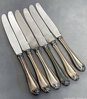 Front of six vintage butter knives arranged side by side showing all blades and handles.