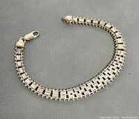 Full view of the silver bracelet laid flat showing full 8 inch span, linked design with bead accents along edges against a grey leather background.