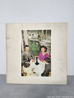 Front cover of Led Zeppelin Presence album showing family sitting at table by a marina with boats, showing minor wear and discoloration.