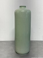 Front view of tall narrow ceramic mint green vase showing glossy surface and signature on base.