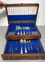 Open two-tier wood case with blue felt lining showing assorted Birks Regency Plate flatware pieces