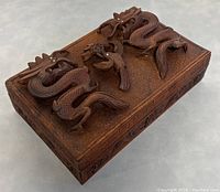 Picture of vintage Chinese wooden trinket box showing 3D carved dragons and bird motifs on lid from an angled top view.