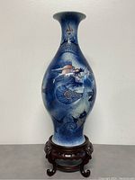 Front view of the blue and white ceramic vase with hand painted Chinese dragon design placed on the carved wooden display stand.